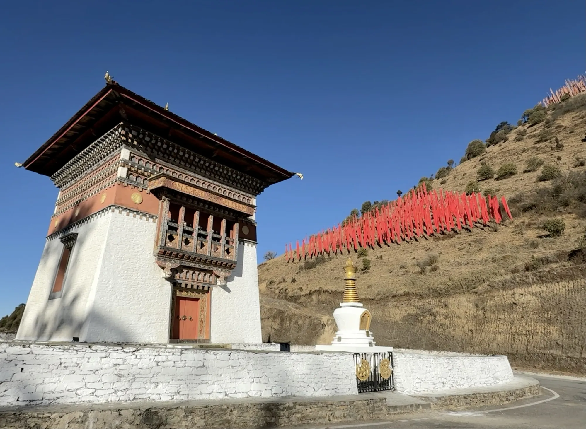 A temple and chorten on a Bhutanese hillside hung with prayer flags